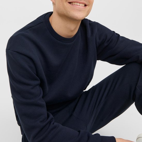 Man met donkerblauwe, effen sweater met ronde hals en geribde boorden.