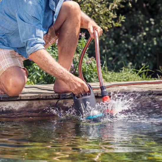 Man gebruikt een vuilwaterpomp met tuinslang in een vijver.