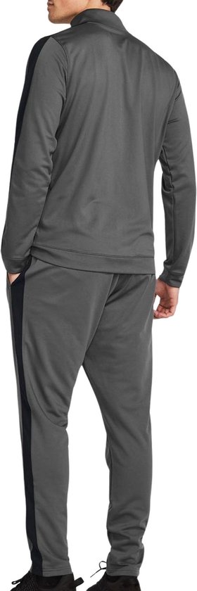 Achterkant van een grijs Under Armour trainingspak met zwarte strepen langs de buitenkant van de benen en mouwen.