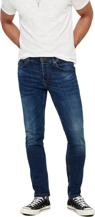 Man in skinny jeans met donkere wassing, wit t-shirt en zwarte sneakers, van voren gezien.