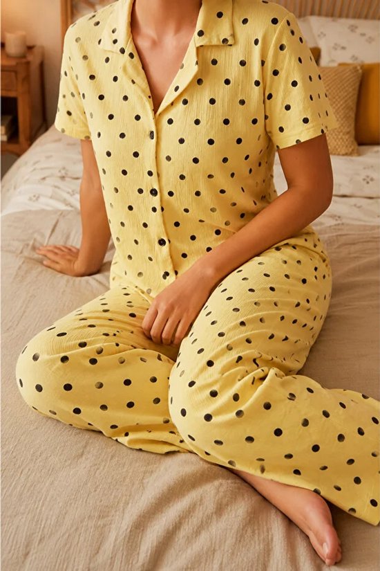 Model zittend in een gele pyjama met korte mouwen en lange broek, gedecoreerd met zwarte polkadots.