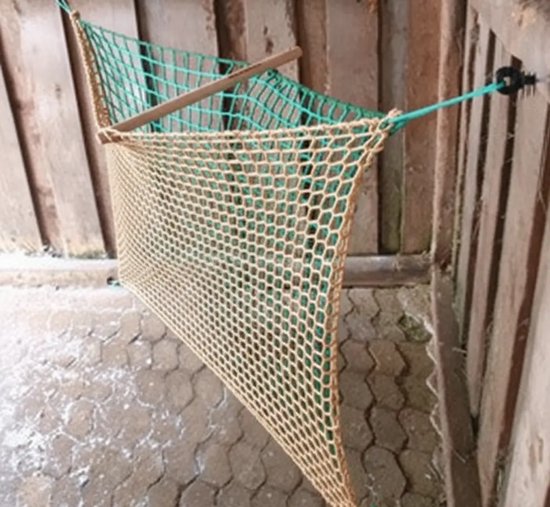 Een groen hooinet met beige maaswijdte hangt aan een houten paal.