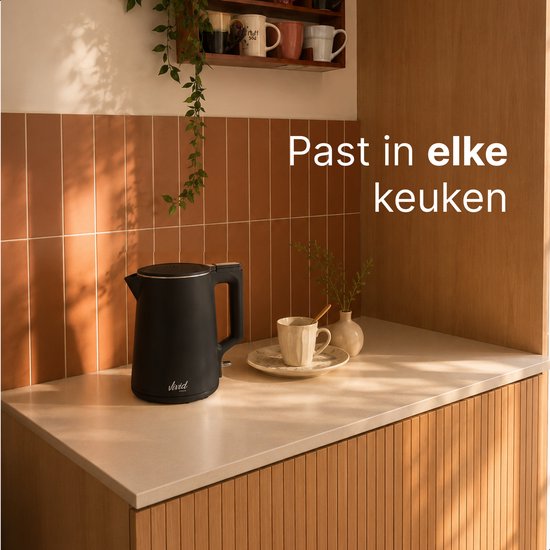 Zwarte waterkoker op een aanrecht in een keuken. Ernaast een mok en decoratieve vaasjes.