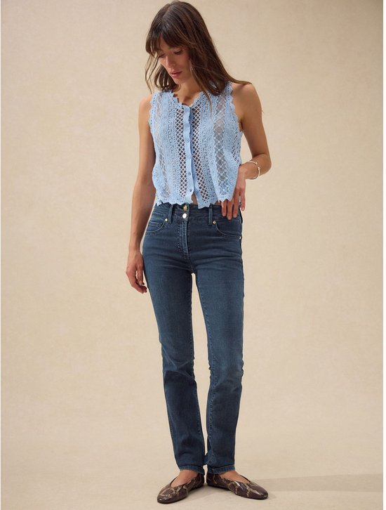 Model in een lichtblauwe kanten top en donkerblauwe slim jeans met rechte pijpen.