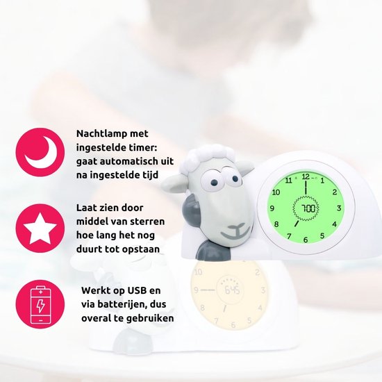 Witte schaap wekker met blauw hoofd. Groen display toont 7:00. Tekst en iconen: nachtlamp, sterren tellen af, USB/batterij.