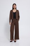 Model in een bruine wijde broek en bijpassend cropped jasje, met een zwarte top eronder. Bruine puntige schoenen.