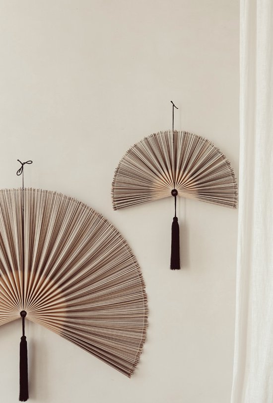 Twee decoratieve bamboewaaaiers met zwarte kwasten aan de muur, één groter dan de ander.