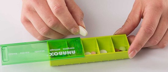 Mains remplissant une boîte à pilules Anabox jaune avec des pilules blanches et colorées.