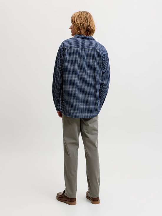 Man draagt grijze chino, wit T-shirt en blauw geruit overhemd, van achteren gezien.
