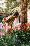 Meisje met opgestoken haar kijkt naar een roodbruin insectenhotel in een tuin met bloemen.