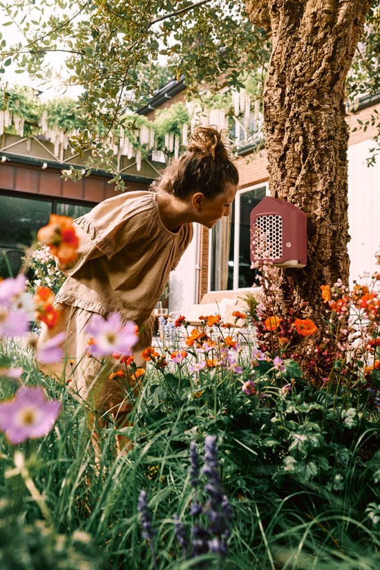 Meisje met opgestoken haar kijkt naar een roodbruin insectenhotel in een tuin met bloemen.