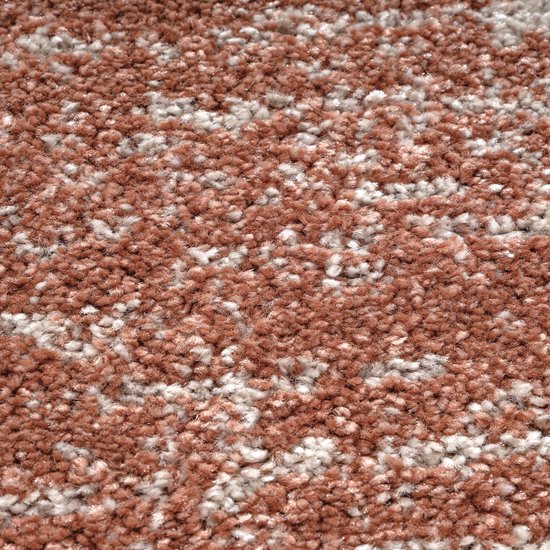 Close-up van een rond vloerkleed met een mix van terra oranje en crèmekleurige vezels.