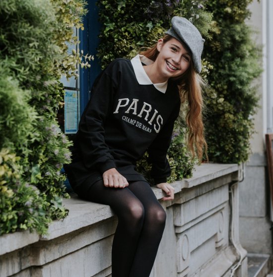 Meisje in zwart jurkje met 'PARIS CHAMP DE MARS' opdruk, witte kraag en grijze baret.