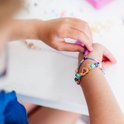 Kind maakt een kleurrijke armband met kralen en een unicorn bedel.