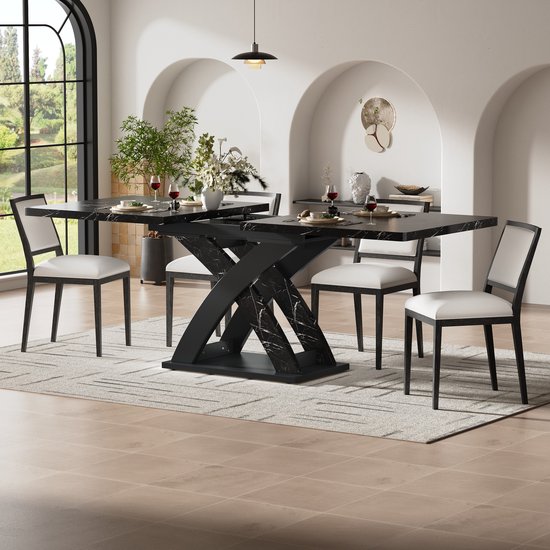 Zwarte uitschuifbare eettafel met marmerprint en X-vormig onderstel, omringd door vier witte stoelen met zwart frame.