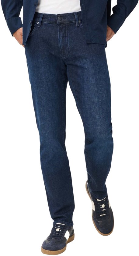 Model draagt donkerblauwe slim fit jeans met blauw overhemd en sneakers.