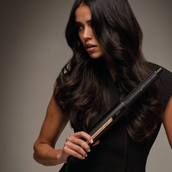 Model met lang, donkerbruin, golvend haar, houdt de zwarte MAE Airstyler II vast met gouden details.