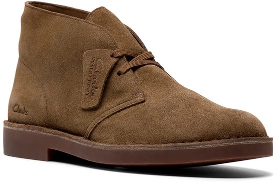 Zij aanzicht van een bruine suède woestijnschoen met veters, rubberen zool en label 'Clarks Desert Boot'.