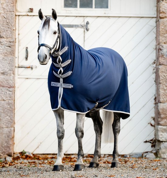 Grijs paard in stand, voorzien van een Horseware Amigo jersey navy zweetdeken met halsstuk.