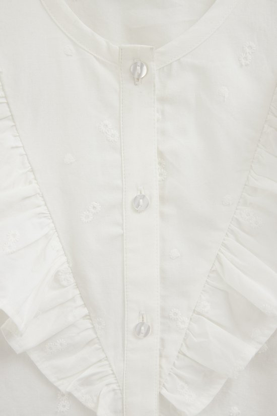 Close-up van een witte blouse met ruches, knopen en een geborduurde bloemetjesprint.