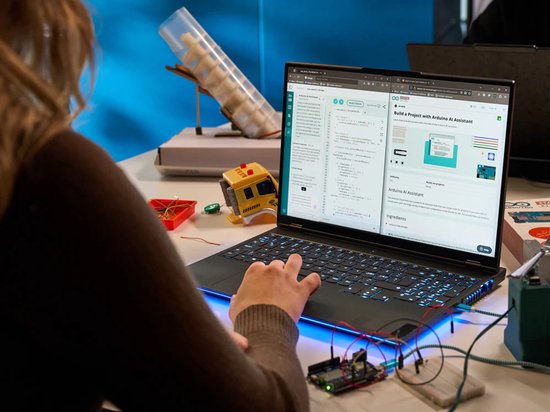 Een persoon gebruikt een laptop waarop de Arduino IDE-website wordt weergegeven, met elektronica en een Arduino-bord op de tafel.
