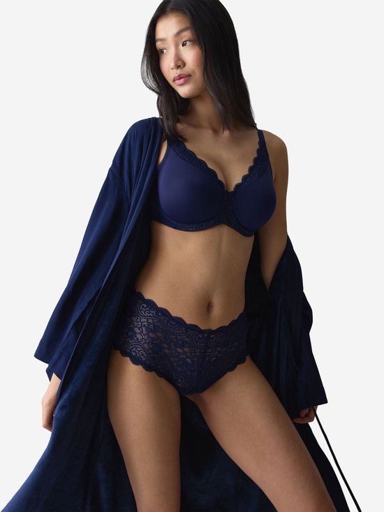 Model in een donkerblauwe beha, slip en bijpassende ochtendjas. De beha en slip hebben kanten details.