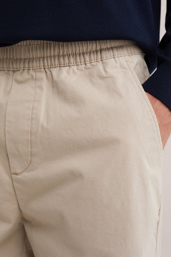 Detail van de steekzakken van een beige chino met een elastische tailleband.