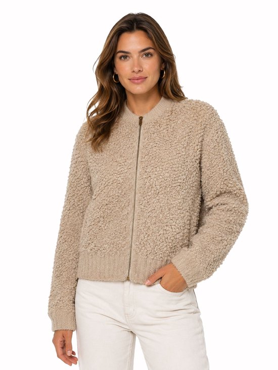 Model draagt een beige teddy bomberjack met ritssluiting en witte broek.