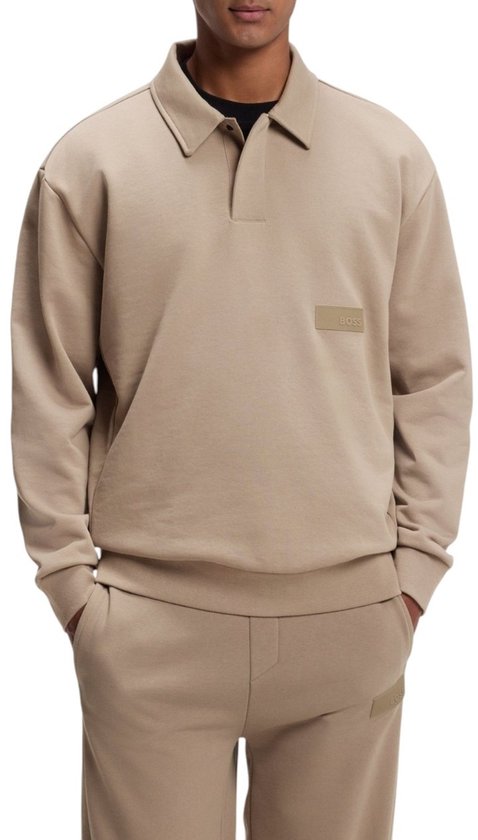 Model draagt een beige BOSS-polo met kraag, lange mouwen en logo-badge, gecombineerd met joggingbroek.