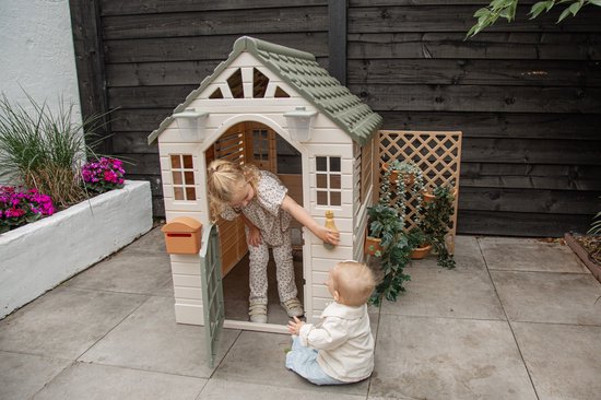 Een meisje in een speelhuisje met een baby ervoor, buiten op een betegeld terras.