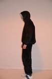 Zwarte oversized hoodie en joggingbroek met rode 'S' logo's, profiel weergave. Model draagt witte sneakers.