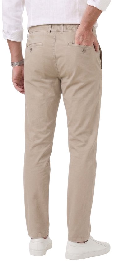 Man van achteren gezien, draagt een beige chino broek met een witte linnen blouse en witte sneakers.