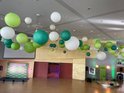Veel ronde papieren lampionnen in wit, lichtgroen en donkergroen hangen aan het plafond. Op de achtergrond een podium met een scherm.