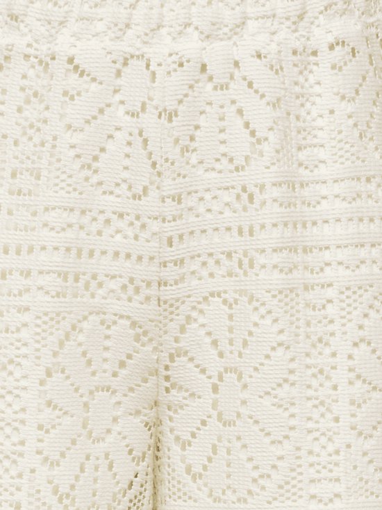 Close-up van het ingewikkelde kanten bloemenpatroon van de crèmewitte broek.