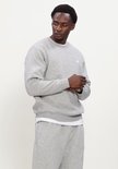 Man in een lichtgrijze New Balance sweater met kleine NB-logo op de borst.
