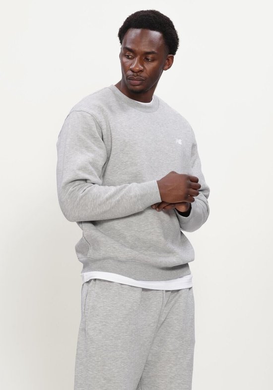 Man in een lichtgrijze New Balance sweater met kleine NB-logo op de borst.
