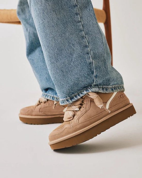 Lage beige UGG sneakers met een dikke zool, gedragen met spijkerbroek.