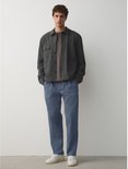 Model in een blauwe chino met een ruimvallende, taps toelopende pasvorm, gecombineerd met een grijs jack.