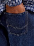 Detail van de achterzak van een donkerblauwe jeans met gele stiksels.