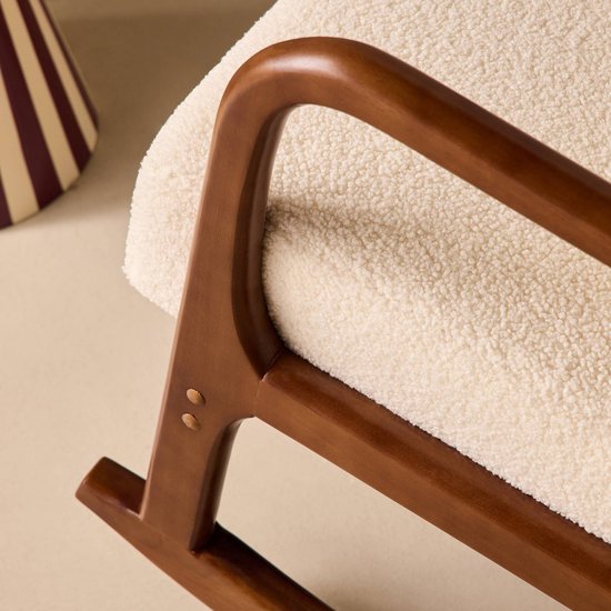 Detail van een schommelstoel met een walnootkleurig houten armleuning en crèmekleurige bouclé bekleding.