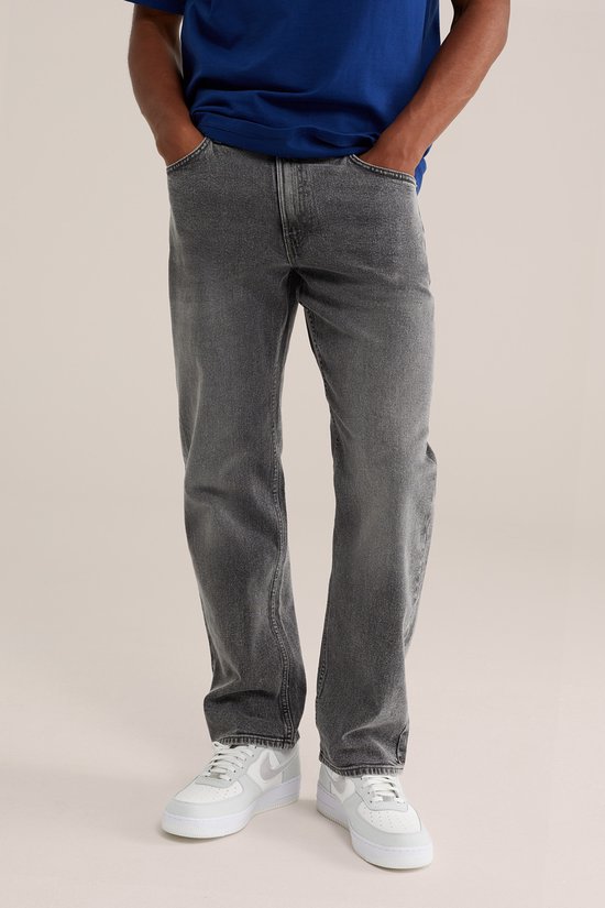 Model staat frontaal, draagt blauwe T-shirt en grijze jeans. Grijze trui om de nek.