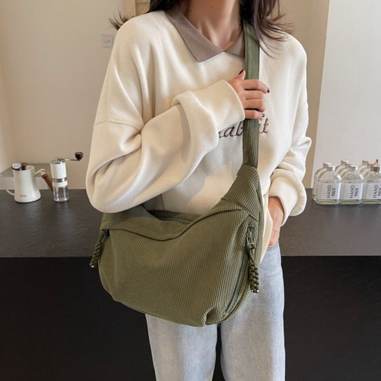 Groene corduroy crossbodytas gedragen door een model, met gedetailleerde ritssluitingen en verstelbare band.