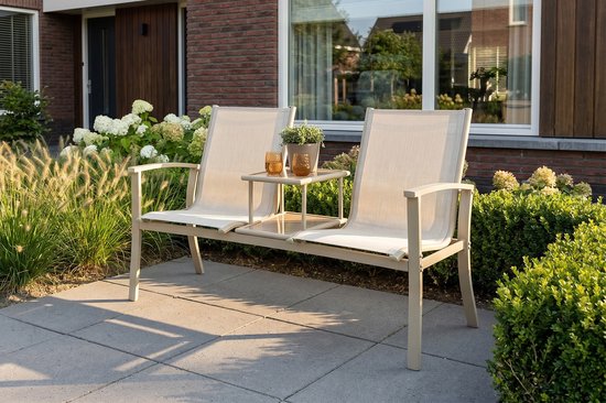 Beige aluminium tuinbank met stoffen zittingen en middenplateau, staand op een terras bij een bakstenen muur.