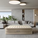 Un matelas pneumatique Intex posé au sol dans un salon moderne avec un grand canapé et des plantes.