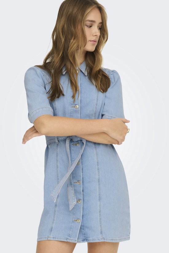 Model draagt een lichtblauwe spijkerjurk met korte, pofmouwtjes, een knoopsluiting en een ceintuur.