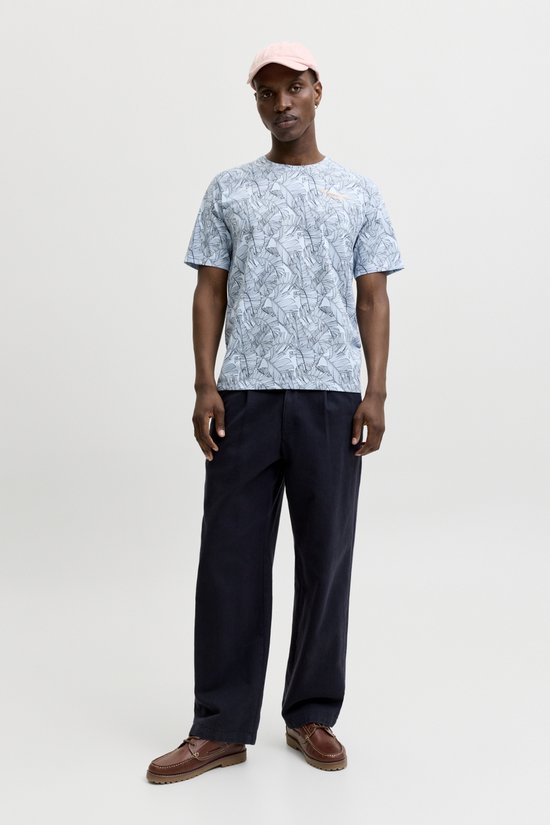 Man draagt een lichtblauwe T-shirt met bananenbladerenprint, oranje tekst en donkerblauwe broek.