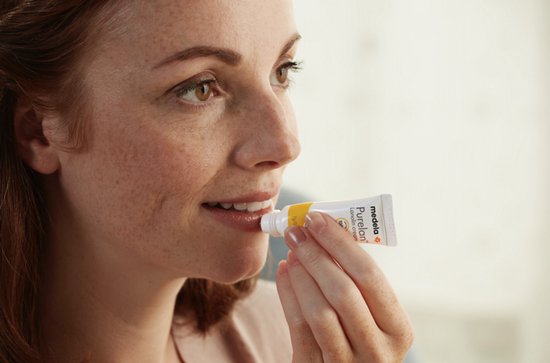 Een vrouw brengt Medela Purelan Lanolin cream aan op haar lippen.