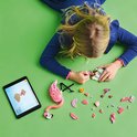 Meisje bouwt een roze LEGO flamingo, met onderdelen en instructies op een tablet.