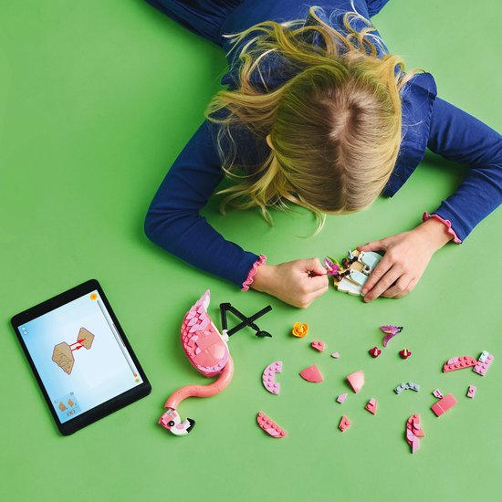 Meisje bouwt een roze LEGO flamingo, met onderdelen en instructies op een tablet.