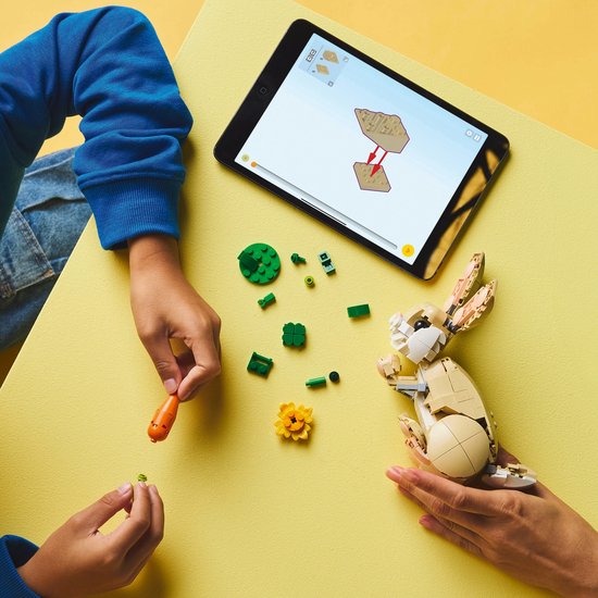 Enfants construisent un lapin LEGO avec carotte et fleur, tablette avec instructions.